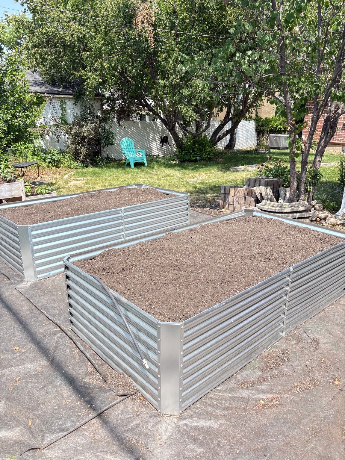Two rectangular metal raised garden beds filled with level soil in a backyard.